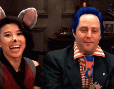 a man and a woman are sitting next to each other and smiling . the woman is wearing a mouse costume .