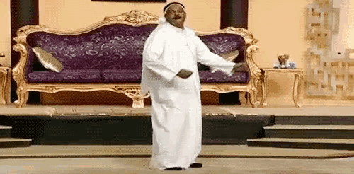 a man in a white robe is dancing in front of a purple and gold couch