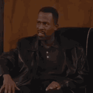 a man is sitting in a chair wearing a black leather jacket and a black shirt .