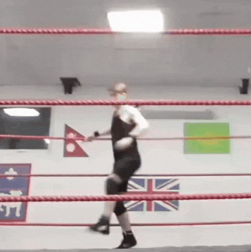 a man is standing in a boxing ring with flags on the wall .