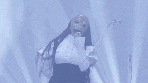 a woman wearing a mask and white gloves sings into a microphone
