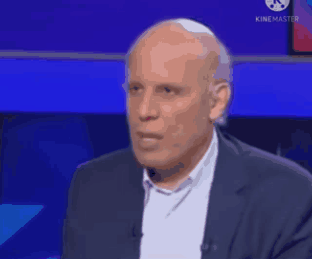 a bald man in a suit is sitting in front of a blue screen .