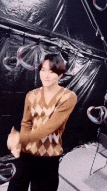 a man in a plaid sweater is standing in front of soap bubbles .