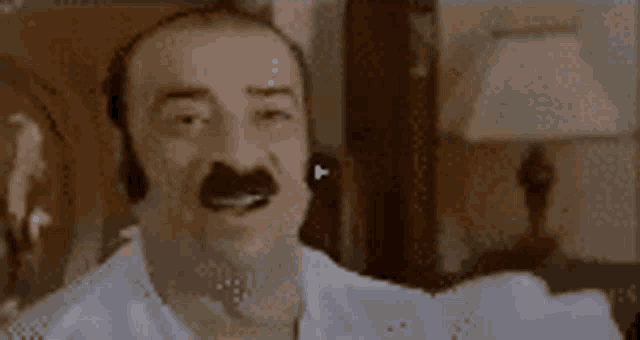 a man with a mustache and a white shirt is making a funny face .