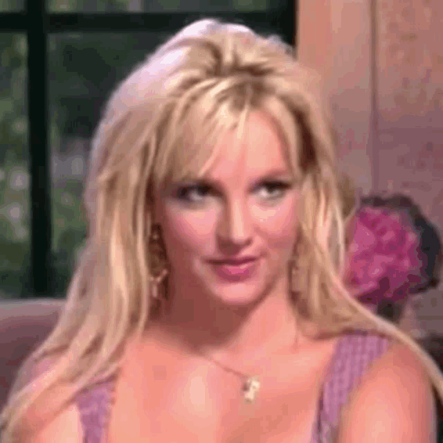 britney spears is sitting on a couch wearing a purple dress and necklace .