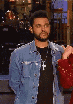 a man wearing a black shirt and a denim jacket with a cross necklace