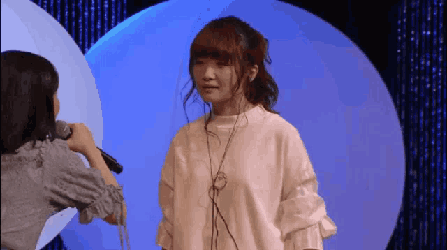 a woman in a white shirt is holding a microphone while another woman looks on