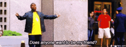 a man in a yellow shirt is standing in front of a building and says does anyone want to be my friend ?