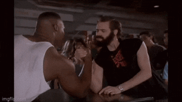 a man with a beard is arm wrestling another man at a bar .