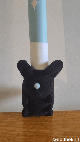 a black stuffed animal is sitting on a wooden table next to a blue and white cylinder with a diamond on it