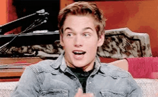 a young man wearing a denim jacket is sitting on a couch with his mouth open