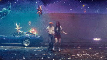 a man and a woman are dancing in a parking lot with a car in the background