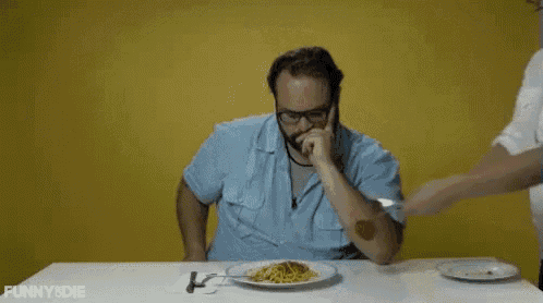 a man in a surgical gown is cutting a plate of spaghetti with a knife and fork .