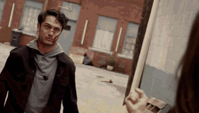 a man with blood on his face stands in front of a brick building