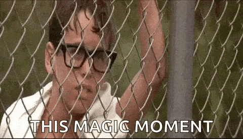 a man wearing glasses is standing behind a chain link fence and saying `` this magic moment '' .