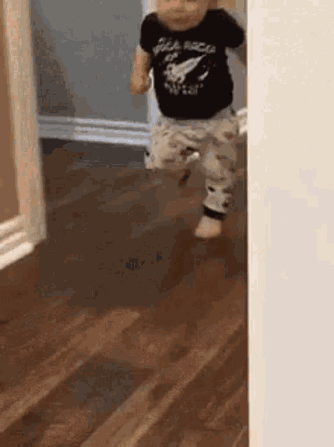 a baby is walking on a wooden floor in a room .