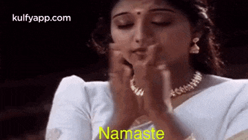 a woman in a white saree is praying with her hands folded in prayer .