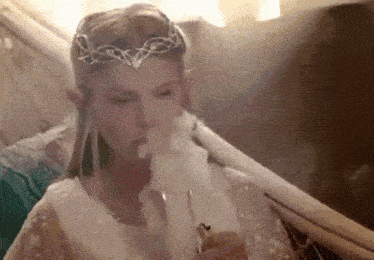 a woman in a white dress is smoking a cigarette while wearing a crown .