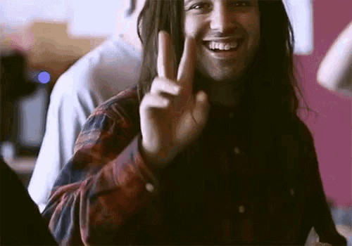 a man with long hair is smiling and giving the peace sign