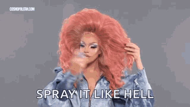 a drag queen with a very large pink wig is spraying her hair .