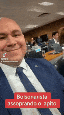 a man in a suit and tie is smiling in a room with other people