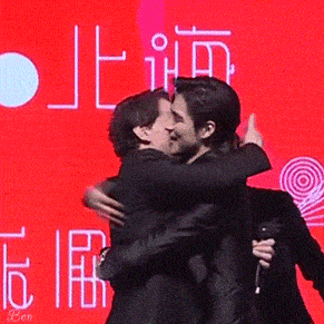 two men are hugging each other on a stage in front of a red screen .