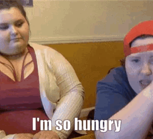 two women are sitting at a table and one is saying i 'm so hungry