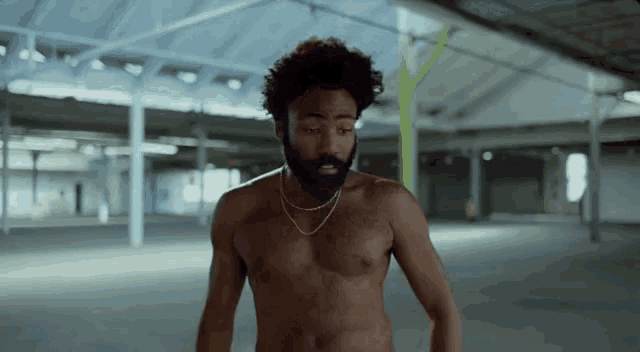 a shirtless man with a beard is standing in a warehouse