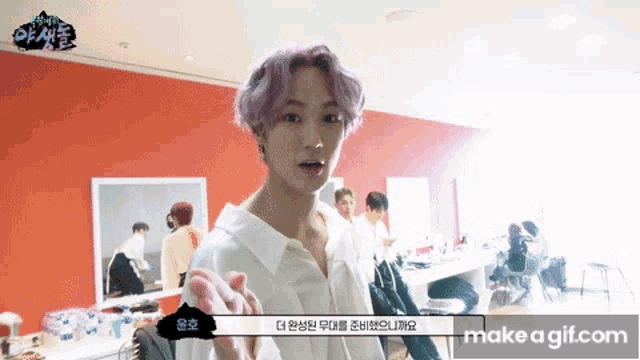 a man with purple hair is standing in front of a red wall and talking to someone
