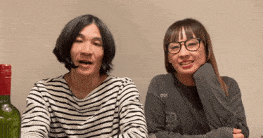 a man and a woman sitting next to each other with a bottle of green liquid in the background