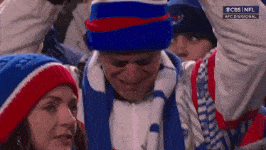 a man wearing a blue hat and scarf is crying in a crowd .