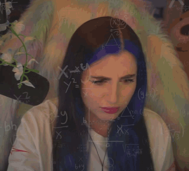 a woman with purple hair is sitting in front of a chalkboard with math equations on it