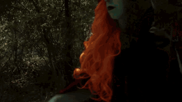a woman with red hair and a cross on her forehead is holding a blue flame