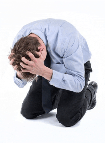 a man in a blue shirt and tie is kneeling down with his hands on his head .