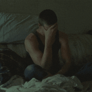 a man sits on a bed with his head in his hands