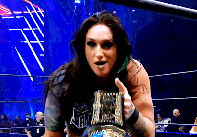 a woman in a wrestling ring holding a trophy that says aew