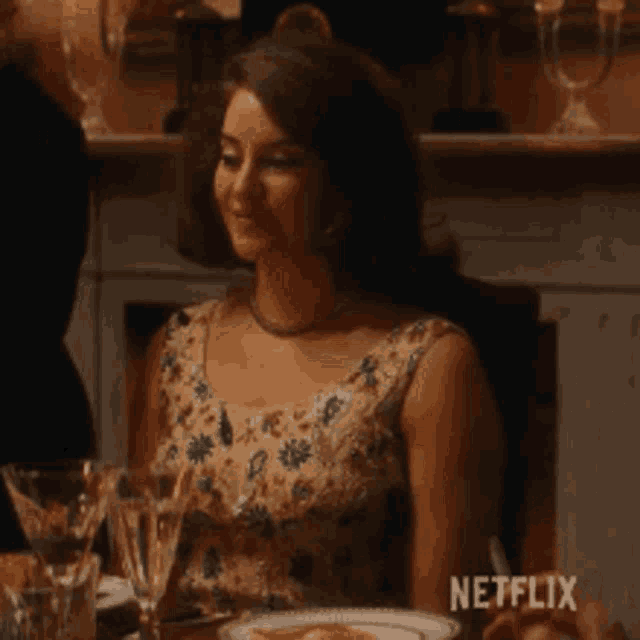 a woman is sitting at a table with a plate of food and wine glasses .