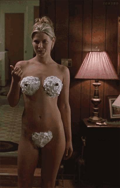 a naked woman with shaving cream on her breasts stands in front of a red lamp
