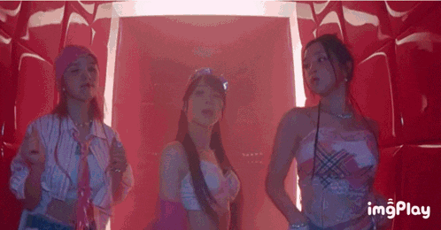 three women are standing next to each other in front of a red wall in a room .