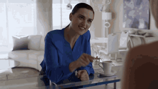 a woman in a blue shirt is sitting at a table with a cup of coffee on it .
