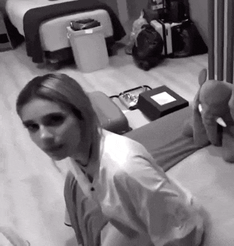 a black and white photo of a woman sitting on a bed in a room .