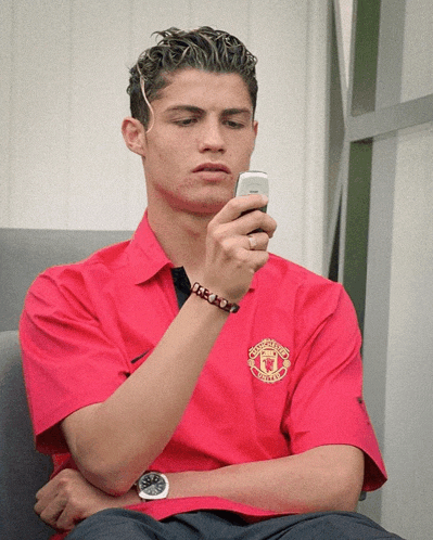 a man wearing a red manchester united shirt is looking at his cell phone