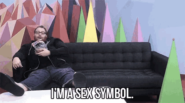 a man is sitting on a couch with his feet on a table and saying i 'm a sex symbol .