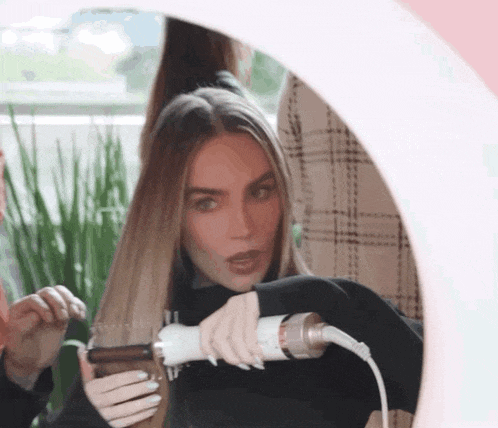 a woman is getting her hair straightened by another woman in front of a mirror