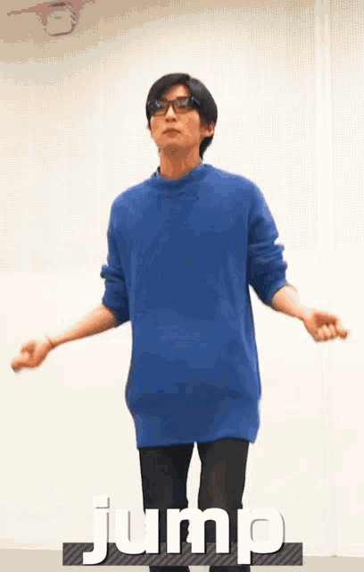 a man wearing glasses and a blue sweater is jumping in the air