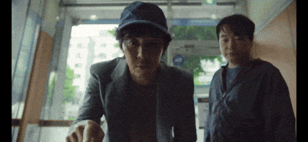 two men are standing next to each other in a hallway . one of the men is wearing a blue hat .