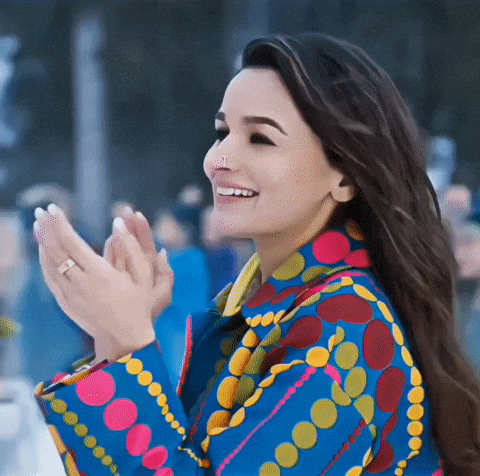 a woman in a colorful jacket is clapping her hands and smiling