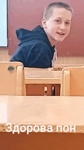 a young boy is sitting at a desk with a foreign language written on the bottom