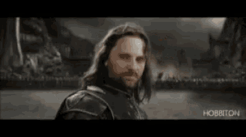 a man with long hair and a beard is standing in front of a sign that says it 's coming home .