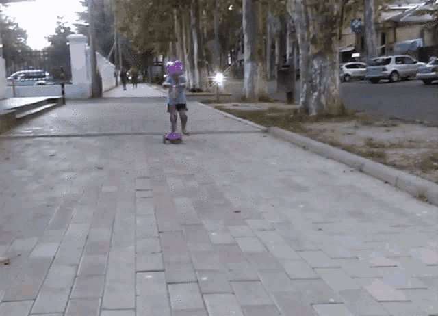 a little girl is riding a scooter on a sidewalk